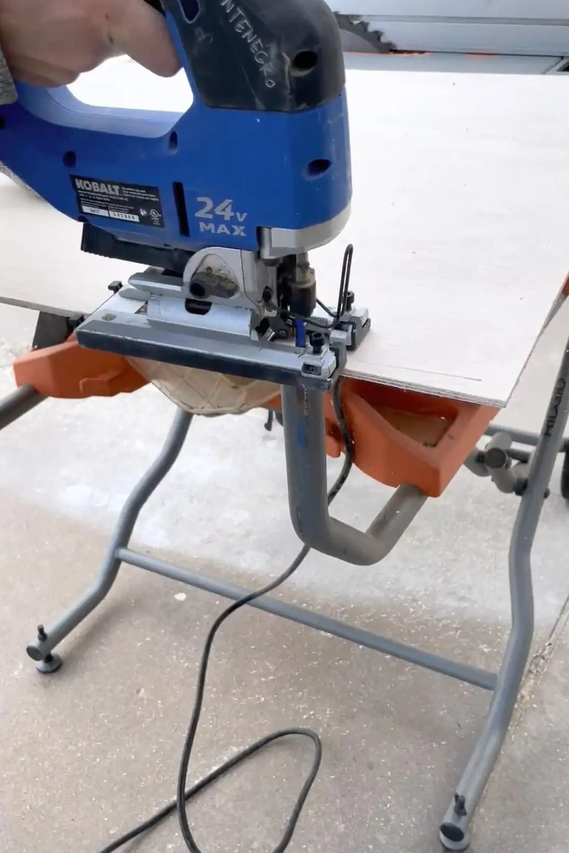 A DIYer uses a blue Kobalt jigsaw to cut plywood on a portable workbench, preparing materials for custom closet shelves.